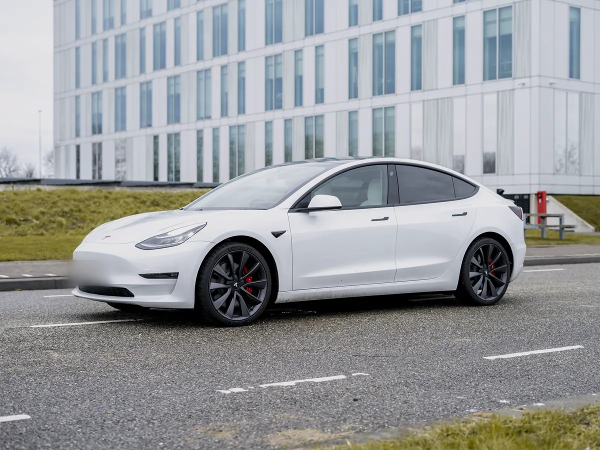 White Tesla Model 3 Performance (2018–2023) with red brake calipers, front three-quarter view on an open road beside a modern office building