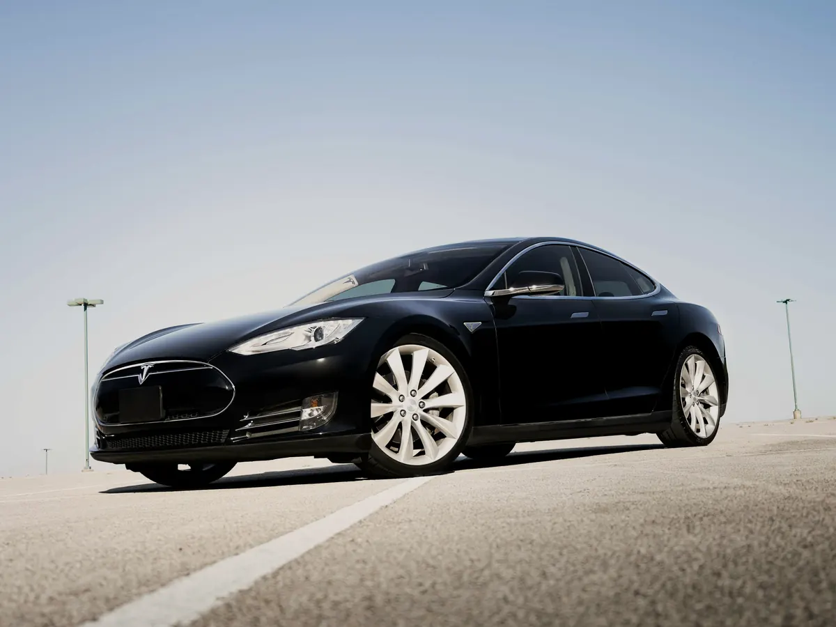 Black Tesla Model S (2012–2016) with the original black nosecone, front three-quarter view in an empty car park under a pale sky