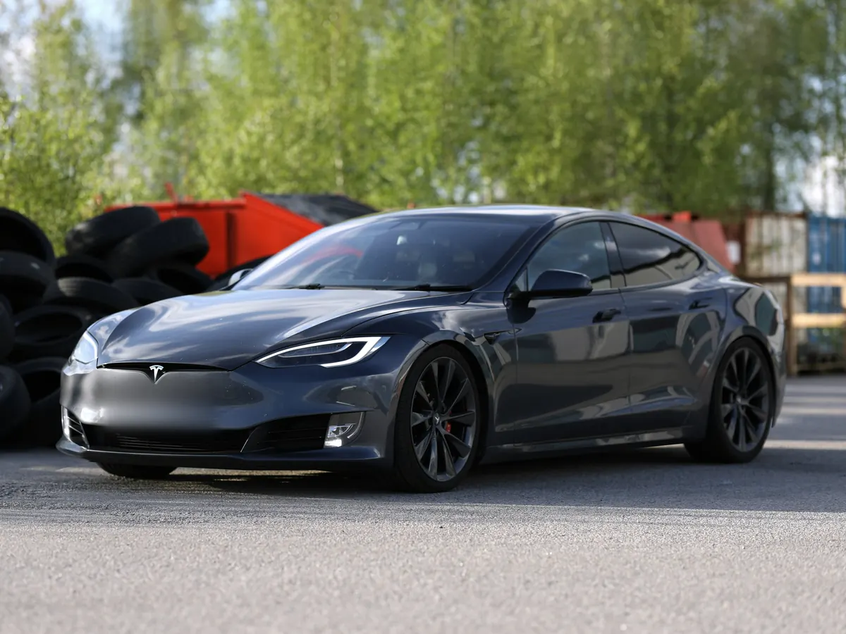 Dark grey Tesla Model S (2016–2020 facelift) with the smooth body-colour nose and red brake calipers, front three-quarter view