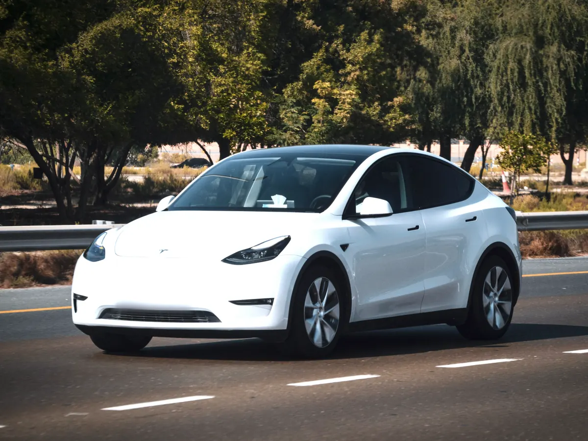 White Tesla Model Y (2020–2024) in front three-quarter view on a highway lined with trees