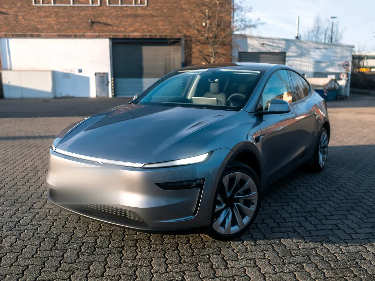 Silver Tesla Model Y “Juniper” (2025+) with its full-width front light bar, front three-quarter view on brick paving