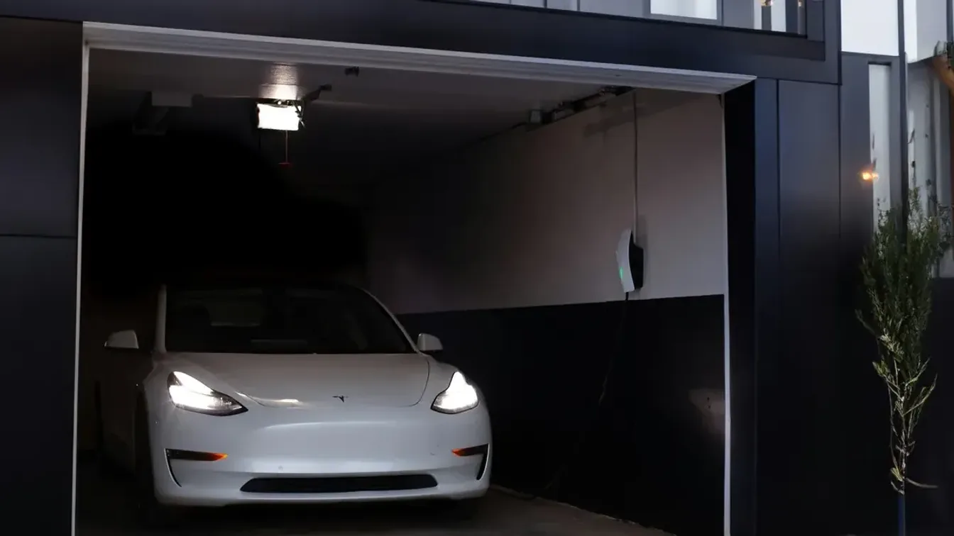 White Tesla Model 3 parked in a modern home garage beside a wall-mounted charger