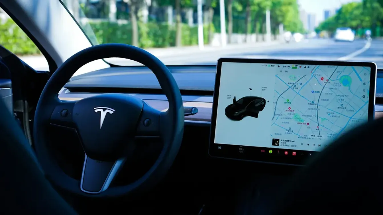 Tesla Model 3 interior, with the steering wheel and centre touchscreen showing a navigation map